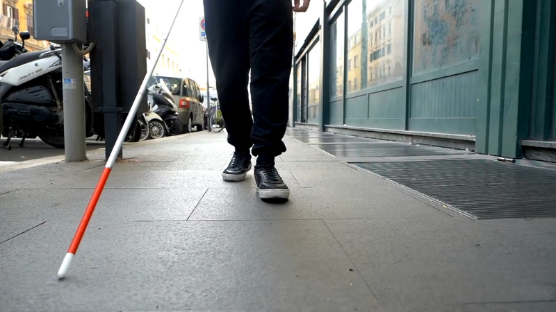 A Person with A White Cane Walking Down a City Sidewalk