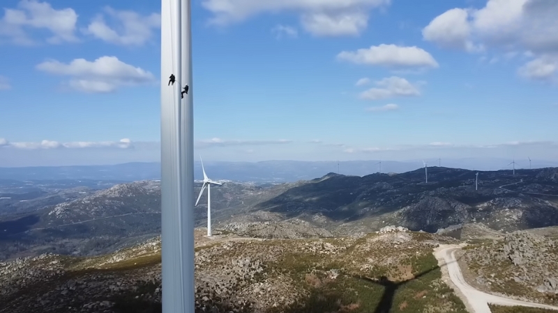 Two Wind Turbine Technicians Are Climbing a Turbine in A Mountainous Area, with Other Turbines Visible in The Distance