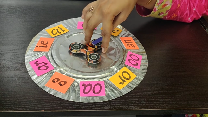 A Hand Spins a Fidget Spinner Placed on A Plate with Colorful Phonetic Letter Combinations to Boost Early Reading Skills