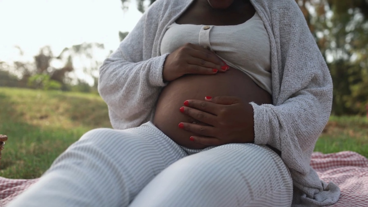 A pregnant woman rests on a picnic blanket in a park